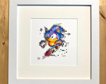 May include: A framed print featuring a pixelated illustration of Sonic the Hedgehog in motion. The artwork showcases the character in blue, yellow, and red hues, with a white border and a white frame. The print is signed in the lower left corner.