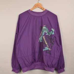 Op de afbeelding: Een paarse longsleeve sweatshirt met een grafische print van een persoon die basketbal speelt. De print is in tinten blauw, groen en zwart.