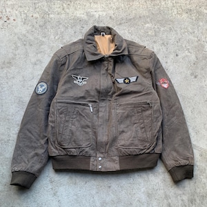 May include: Brown leather bomber jacket with multiple patches and zipper pockets. Features a ribbed collar, cuffs, and hem. Patches include an eagle emblem, a star, and a circular patch. The jacket has a vintage, worn look.