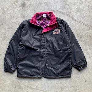 Puede incluir: Una chaqueta reversible negra y rosa con cierre de presión y un parche de logotipo que dice "adidas" en el pecho izquierdo. La chaqueta tiene un estampado geométrico colorido en el interior.