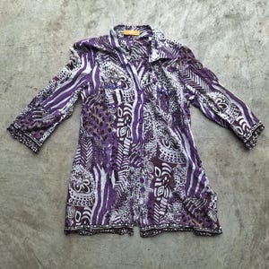 May include: A purple and white patterned button-up shirt with long sleeves. The shirt has a geometric and animal print design.