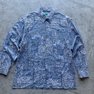 May include: A blue long-sleeved button-down shirt with a white paisley pattern. The shirt has a green label with the text "Green Velvet" on the left side of the collar.