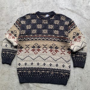 Op de afbeelding: Een bruine, beige en zwarte trui met een ronde hals. De trui heeft een sneeuwvlokkenpatroon.