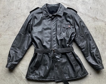 May include: A black leather jacket with a belt and a large pocket on the front. The jacket has a button closure and a collar.