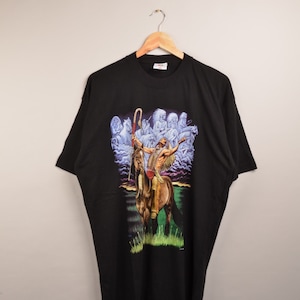 Op de afbeelding: Zwart T-shirt met een grafische print van een indiaan die op een paard rijdt. De print is kleurrijk en toont een zonsondergang op de achtergrond.