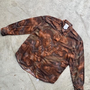 Può includere: Una camicia a maniche lunghe con un motivo astratto marrone e arancione. La camicia ha una tasca sul petto e un colletto classico. Il tessuto sembra leggero e fluido, adatto alle temperature più calde.