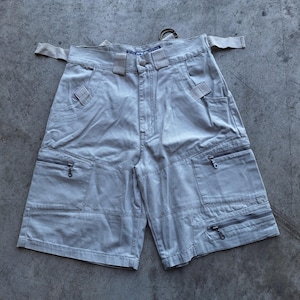 May include: Light gray cargo shorts with multiple pockets and zippers. The shorts have a belt and a button closure. The shorts are made of a durable fabric and are designed for utility and style.