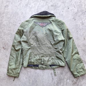 K&ouml;nnte beinhalten: Olivgr&uuml;ne Jacke mit schwarzem Kragen und Harley-Davidson-Logo auf dem R&uuml;cken. Die Jacke hat ein gestepptes Design am unteren R&uuml;cken und einen Knopfverschluss. Die Jacke ist aus leichtem Material gefertigt.