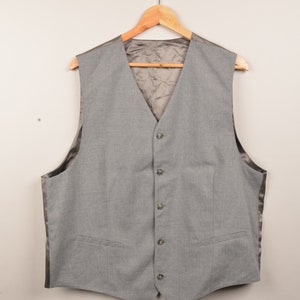 Op de afbeelding: Een grijs vest met een satijnen voering en vijf knopen. Het vest hangt aan een houten hanger.