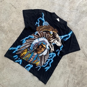 Peut inclure: T-shirt noir avec un motif d'un chef amérindien, d'un loup et d'un aigle, avec des éclairs bleus. Le graphisme est détaillé avec des couleurs vives. Le t-shirt est fait d'une matière douce.