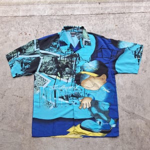 May include: A blue and black short-sleeved button-up shirt with a cartoon character and the text "The Power of Money" printed on it.