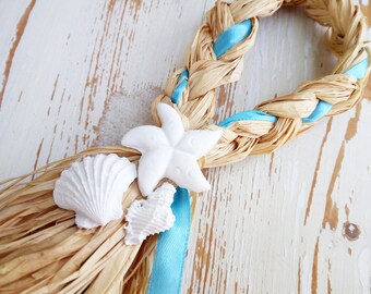 May include: A braided straw wreath with a blue ribbon and white seashells. The wreath is decorated with a white starfish.