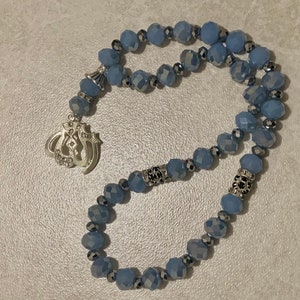 May include: A light blue crystal prayer beads with a silver charm featuring the Arabic word for God. The beads are strung on a silver wire with silver accents.