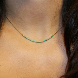 May include: A delicate gold chain necklace with a single row of turquoise beads.