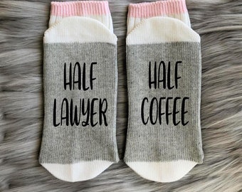 May include: A pair of gray and white socks with pink trim. One sock says "Half Lawyer" and the other says "Half Coffee".