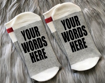May include: A pair of gray and white socks with red trim. The socks have the text "YOUR WORDS HERE" printed on them in black.