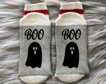 May include: A pair of gray and white socks with red stripes at the top. The socks have a black ghost with the word "BOO" printed on them.