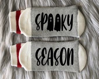 May include: Pair of gray and white socks with red stripes. The socks have the text "Spooky Season" written on them in black.