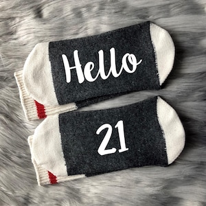May include: A pair of gray and white socks with red trim. One sock says "Hello" and the other says "21".