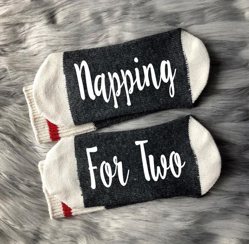 Op de afbeelding: Een paar grijze en witte sokken met rode bies. E&eacute;n sok zegt "Napping" en de andere zegt "For Two".