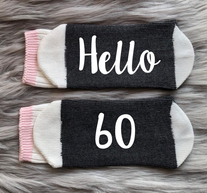 Puede incluir: Un par de calcetines negros y blancos con ribete rosa. Un calcet&iacute;n dice "Hello" y el otro dice "60".
