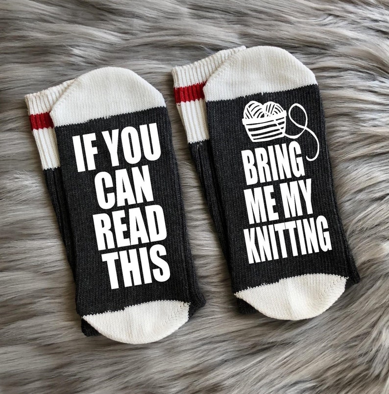Puede incluir: Un par de calcetines grises oscuros con punteras y pu&ntilde;os blancos. Un calcet&iacute;n dice "IF YOU CAN READ THIS" en texto blanco. El otro calcet&iacute;n tiene un gr&aacute;fico de ovillos de lana y el texto "BRING ME MY KNITTING".
