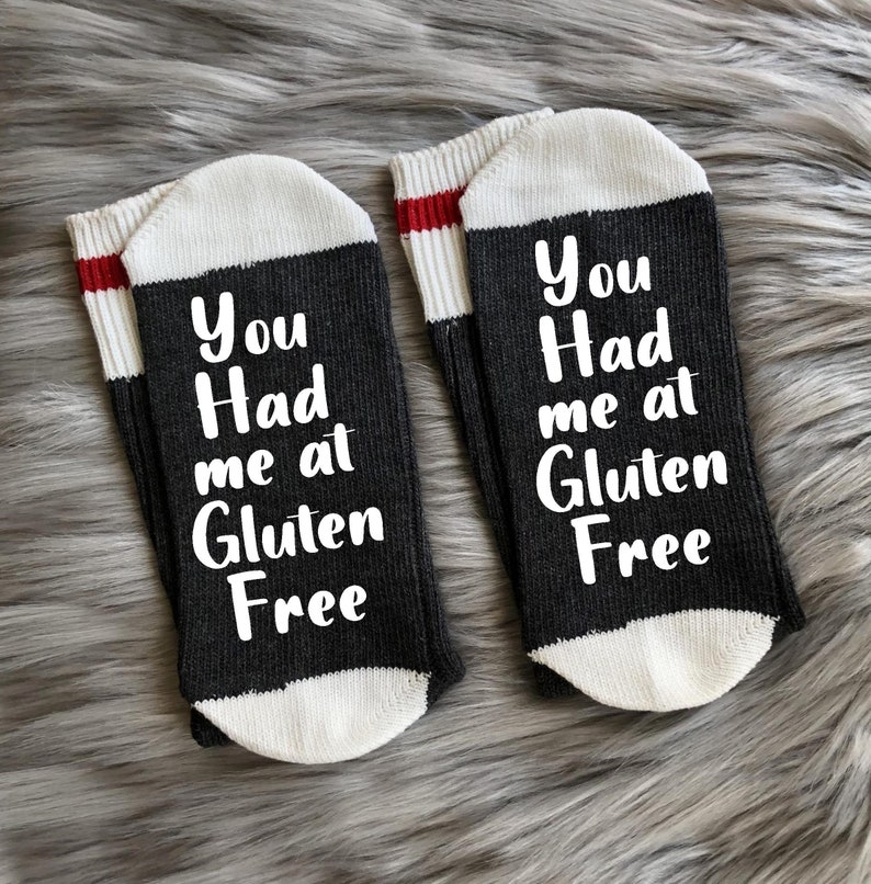 K&ouml;nnte beinhalten: Ein Paar schwarze und wei&szlig;e Socken mit roten Streifen. Die Socken haben den Text "You Had me at Gluten Free" aufgedruckt.