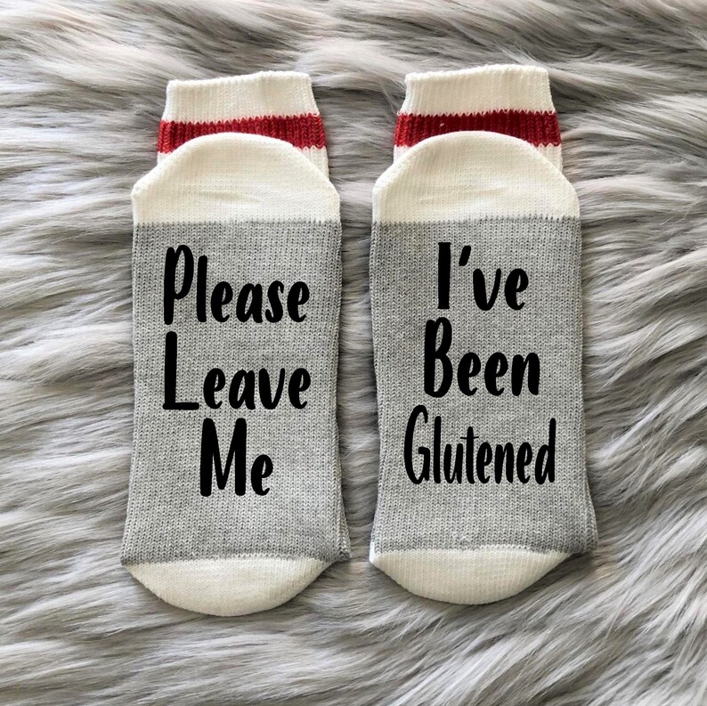 May include: A pair of gray and white socks with red stripes. One sock says "Please Leave Me" and the other says "I've Been Glutened".