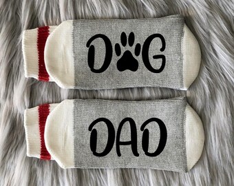 May include: A pair of gray socks with red and white stripes. One sock says "DOG" with a paw print and the other sock says "DAD".