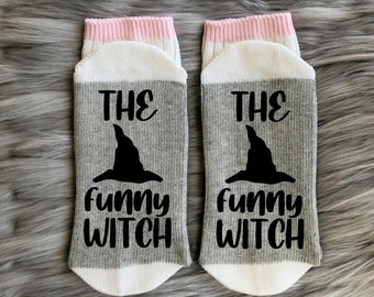 May include: A pair of gray and white socks with a pink trim. The socks have a black witch hat and the text "The Funny Witch" printed on them.