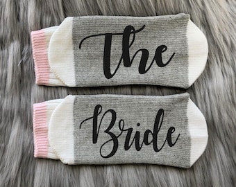 May include: A pair of gray socks with pink trim. One sock says "The" and the other says "Bride".