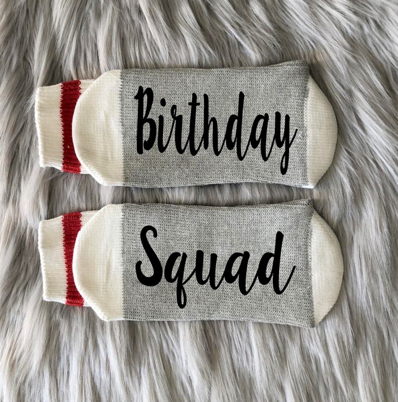 Puede incluir: Un par de calcetines grises con pu&ntilde;os blancos y rayas rojas. Un calcet&iacute;n dice "Birthday" y el otro dice "Squad".