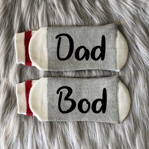 May include: A pair of gray socks with red and white stripes at the top. One sock says "Dad" and the other says "Bod".