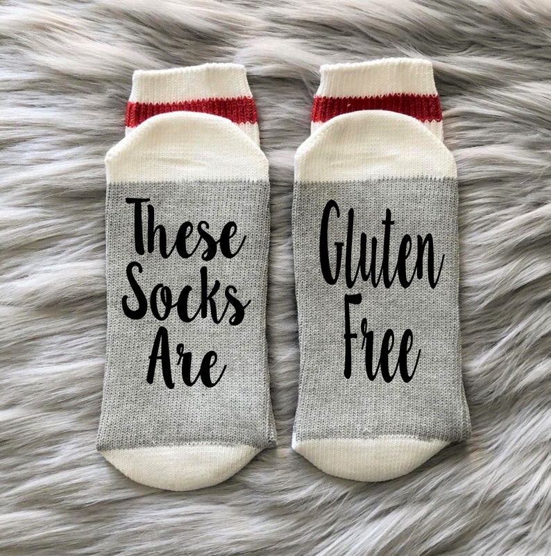 K&ouml;nnte beinhalten: Ein Paar graue und wei&szlig;e Socken mit rotem Besatz. Eine Socke sagt "These Socks Are" und die andere Socke sagt "Gluten Free".
