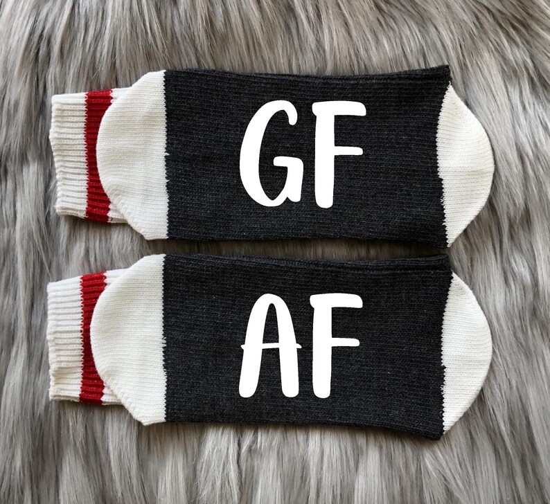 May include: A pair of black socks with white lettering. One sock says "GF" and the other says "AF". The socks have a white cuff with a red stripe.