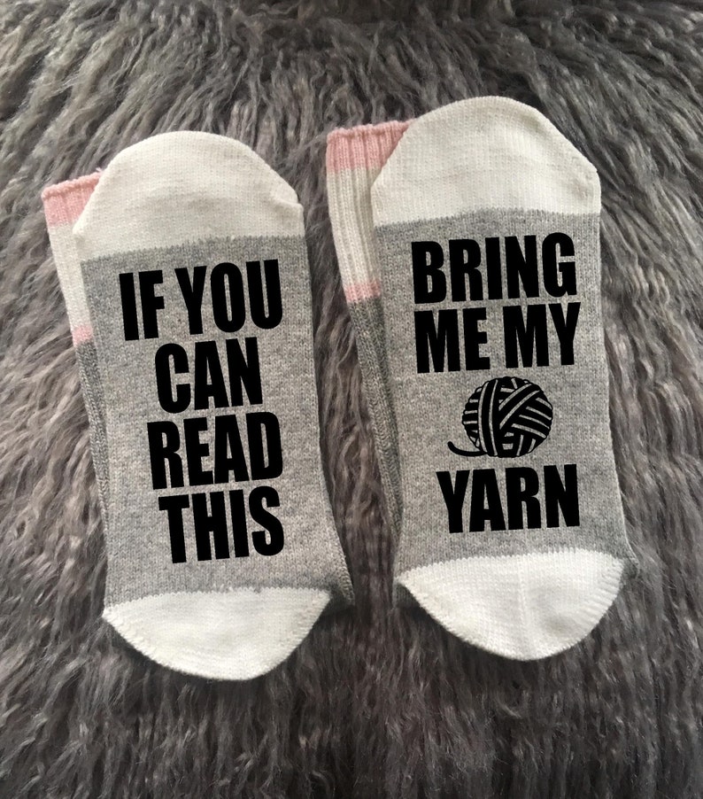 Puede incluir: Un par de calcetines grises con punteras y pu&ntilde;os blancos, y una banda rosa. Un calcet&iacute;n dice "IF YOU CAN READ THIS" en texto negro, y el otro dice "BRING ME MY YARN" con un gr&aacute;fico de ovillo.