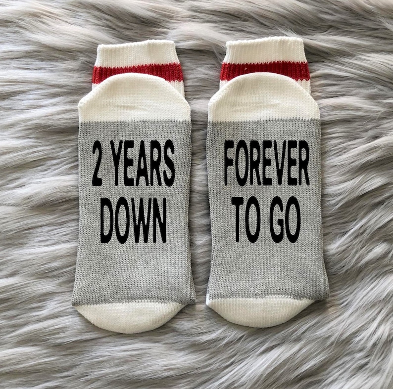 K&ouml;nnte beinhalten: Ein Paar graue Socken mit wei&szlig;en und roten Streifen. Eine Socke sagt "2 Years Down" und die andere sagt "Forever To Go".