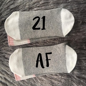 May include: Two gray socks with white and pink stripes. One sock has the number "21" printed on it, and the other sock has the letters "AF" printed on it.