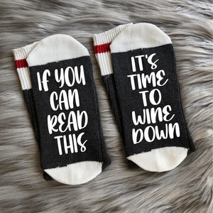 Könnte beinhalten: Ein Paar schwarze Socken mit weißem Text. Eine Socke sagt "Wenn du das lesen kannst" und die andere Socke sagt "Es ist Zeit zum Wein runter".