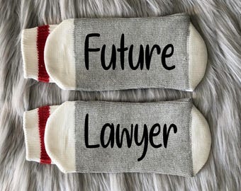 May include: A pair of gray and white socks with red stripes. The socks have the text "Future Lawyer" printed on them.