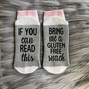 K&ouml;nnte beinhalten: Ein Paar graue und wei&szlig;e Socken mit rosa Besatz. Eine Socke tr&auml;gt den Schriftzug "Wenn du das lesen kannst" und die andere Socke tr&auml;gt den Schriftzug "Bring mir einen glutenfreien Snack".