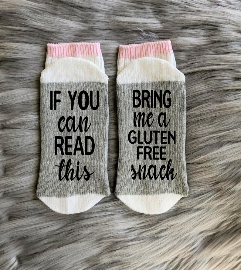 K&ouml;nnte beinhalten: Ein Paar graue und wei&szlig;e Socken mit rosa Besatz. Eine Socke tr&auml;gt den Schriftzug "Wenn du das lesen kannst" und die andere Socke tr&auml;gt den Schriftzug "Bring mir einen glutenfreien Snack".