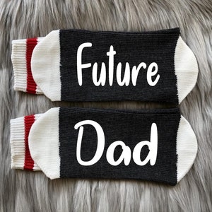 May include: A pair of black socks with white trim and red stripes. One sock says "Future" and the other says "Dad".
