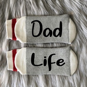 May include: A pair of gray socks with red and white stripes. The socks have the words "Dad" and "Life" written on them in black.