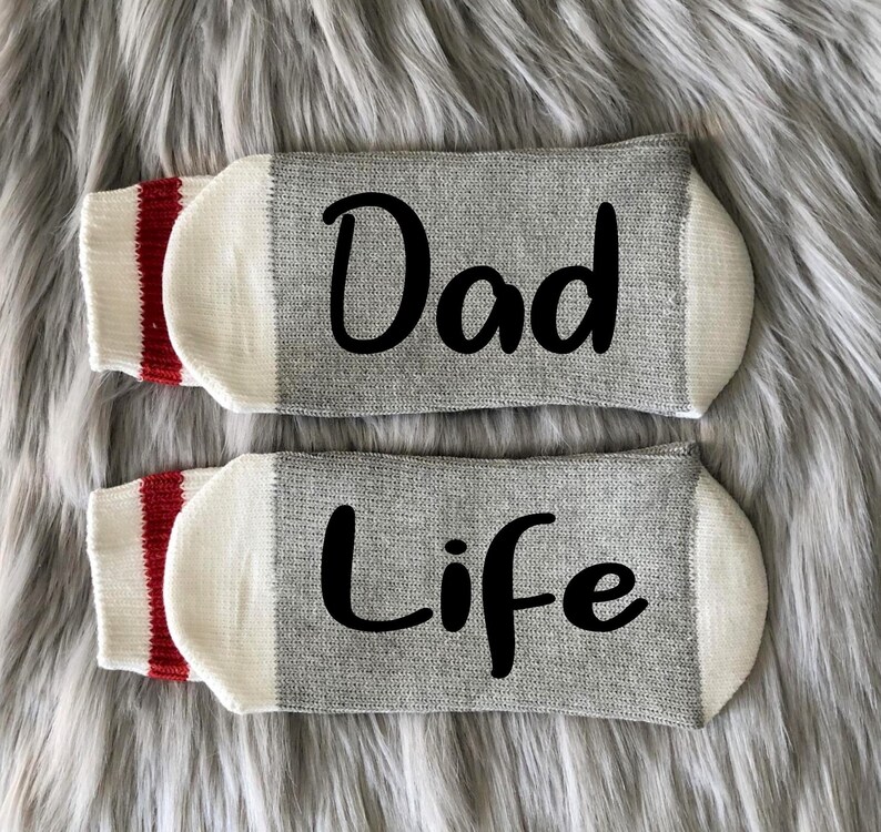 May include: A pair of gray socks with red and white stripes. The socks have the words "Dad" and "Life" written on them in black.