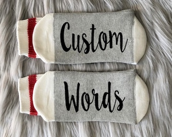 May include: A pair of gray socks with white cuffs and red stripes. The socks have the words "Custom Words" printed on them in black.