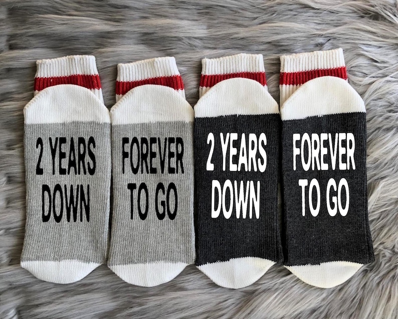 Puede incluir: Cuatro pares de calcetines grises y negros con rayas rojas. Los calcetines tienen el texto "2 Years Down" y "Forever To Go" impreso en ellos.