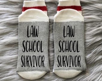 May include: A pair of gray socks with red and white stripes at the top. The socks have the text "Law School Survivor" printed on them.