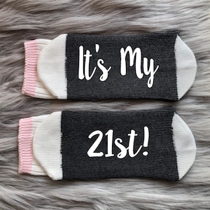 May include: A pair of black and white socks with pink trim. The socks have the text "It's My 21st!" printed on them.