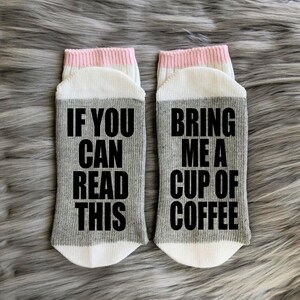 Op de afbeelding: Een paar grijze en witte sokken met roze bies. Op de ene sok staat "Als je dit kunt lezen" en op de andere sok staat "Breng me een kop koffie".